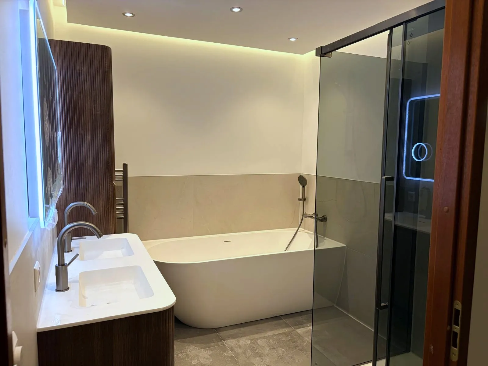Ruime badkamer met een ligbad, een inloopdouche achter glas en een houten wandpaneel