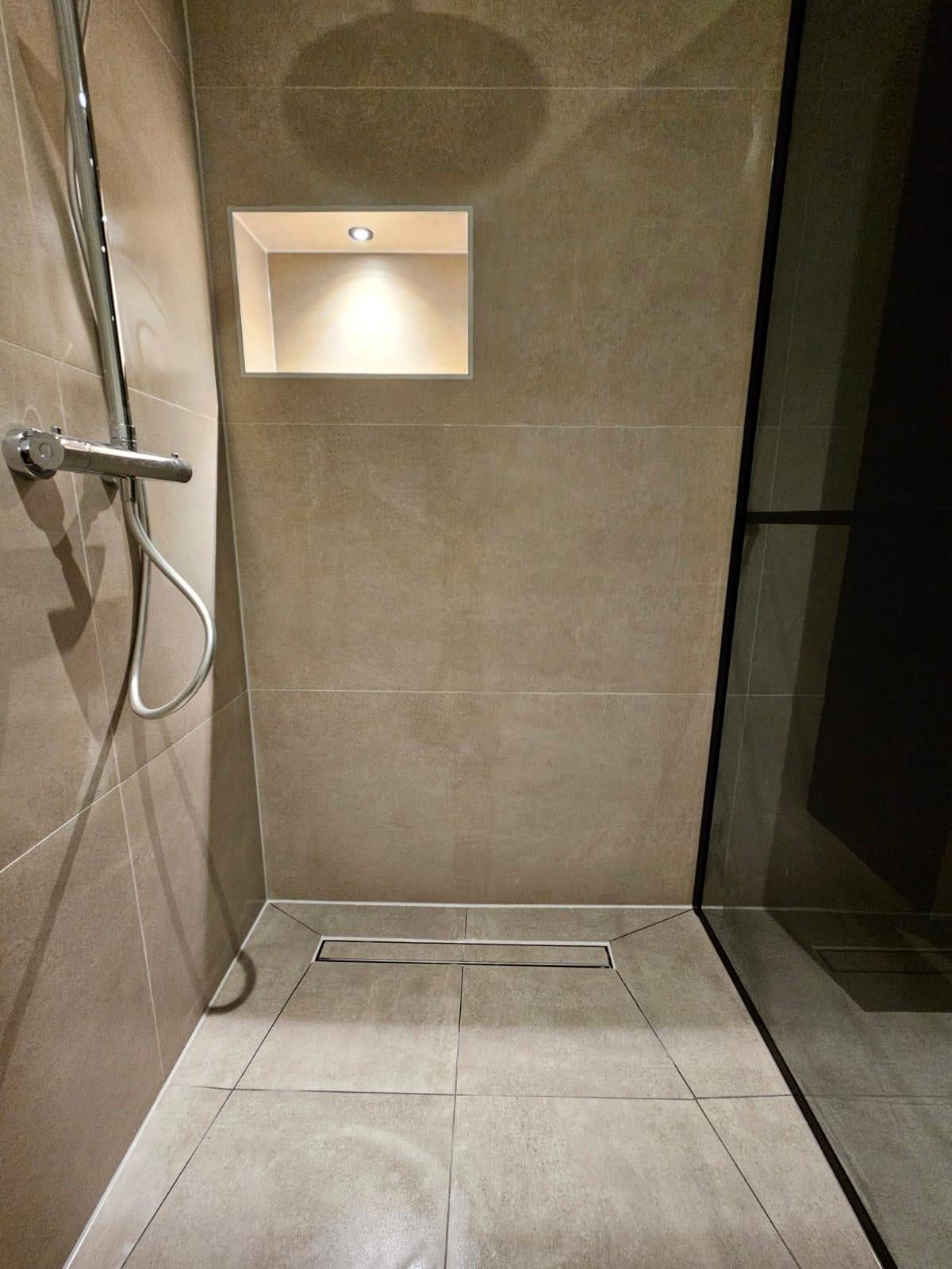Doucheruimte met een verlichte nis in de wand, een chromen doucheset en een afvoergoot in de vloer