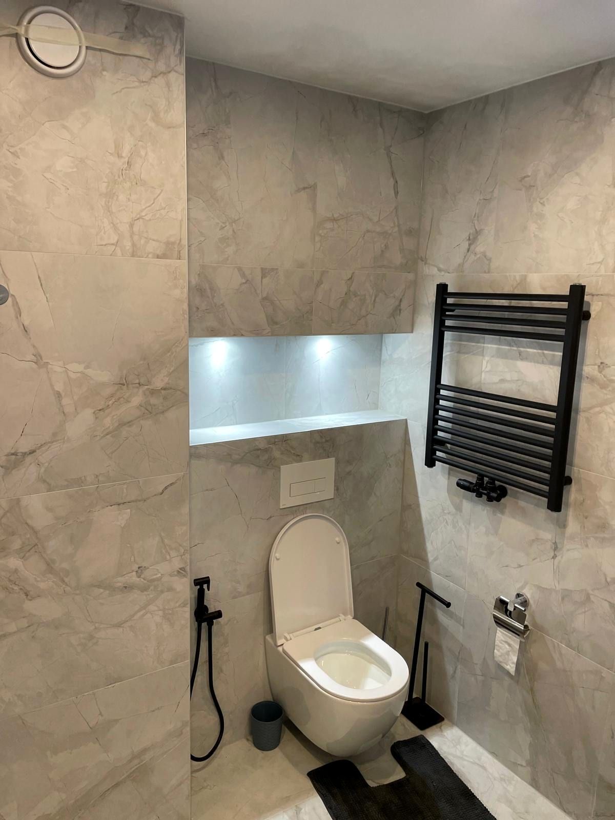 Zwevend toilet tegen grijze marmerlook, met een verlichte schapnis erboven en een zwarte handdoekradiator ernaast