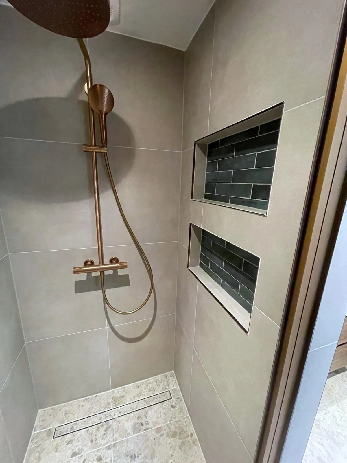 Douche met een messing regendouche en een betegelde nis in de wand