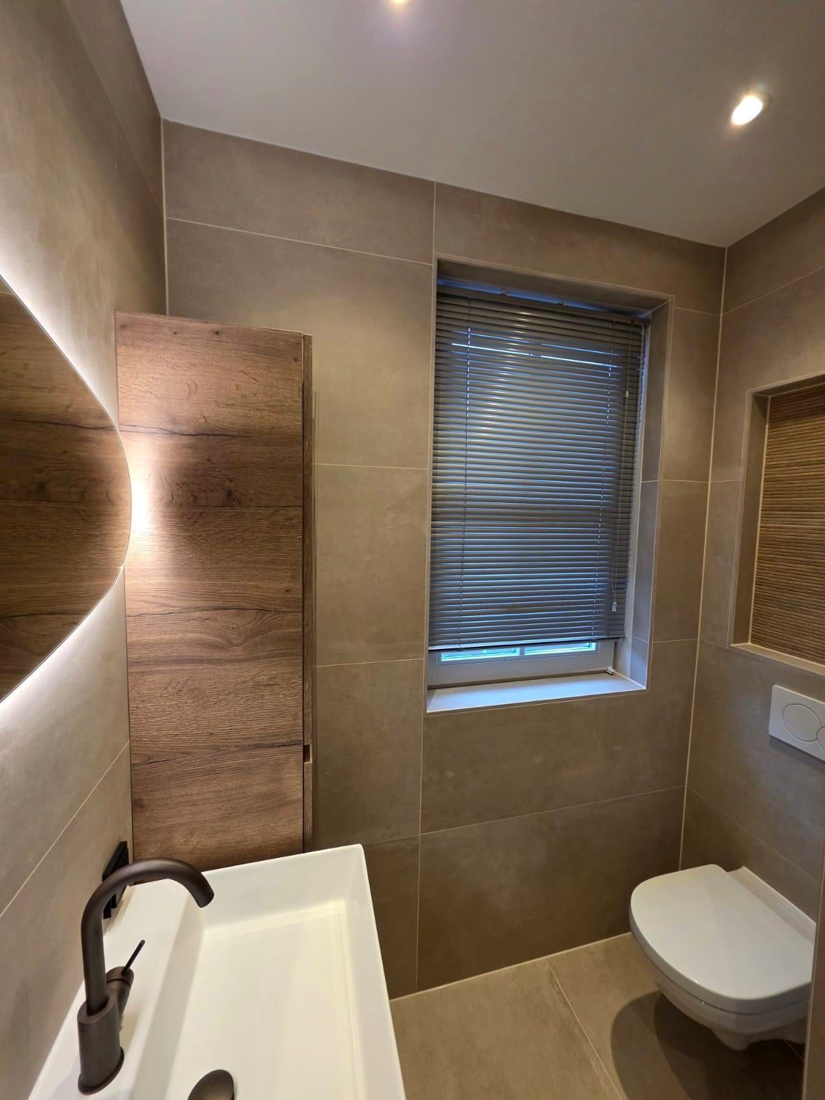 Hoek van de badkamer met een hoge kast in houtlook, het raam met jaloezie en het zwevende toilet ernaast