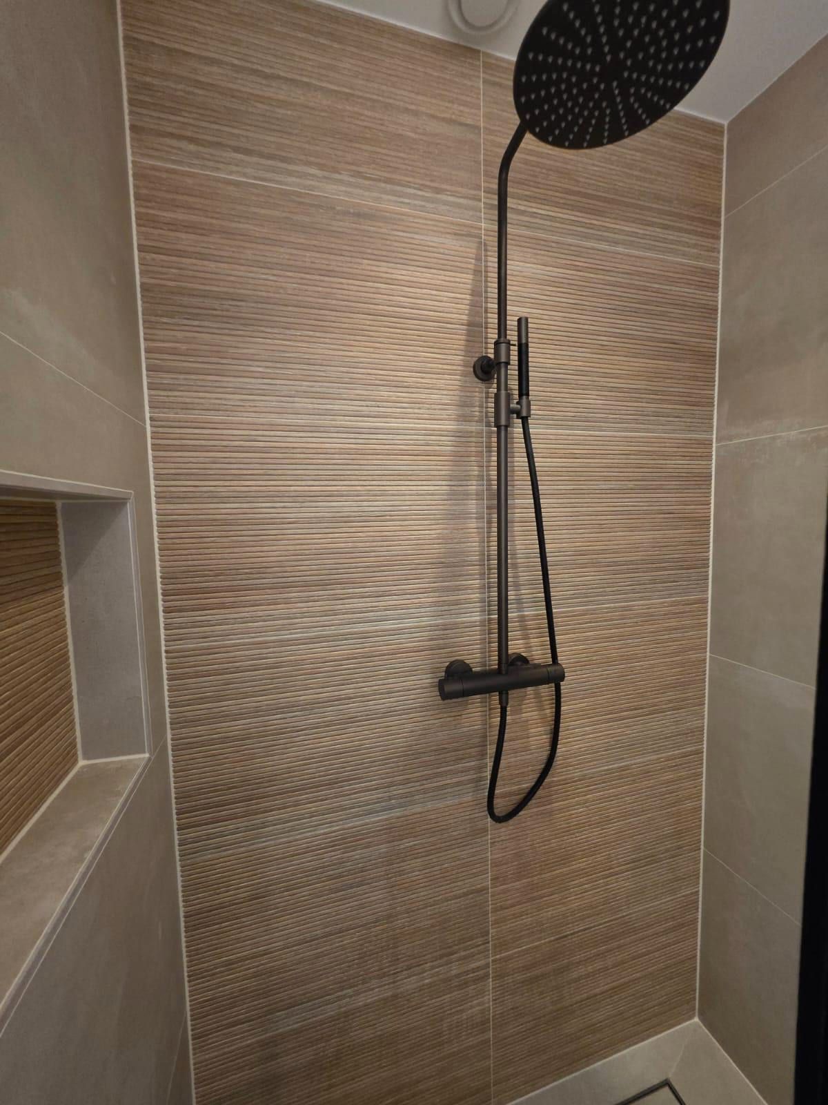 Doucheruimte met een ribbelwand in houtlook, een zwarte regendouche aan een zwarte stang en een handdouche aan een glijstang