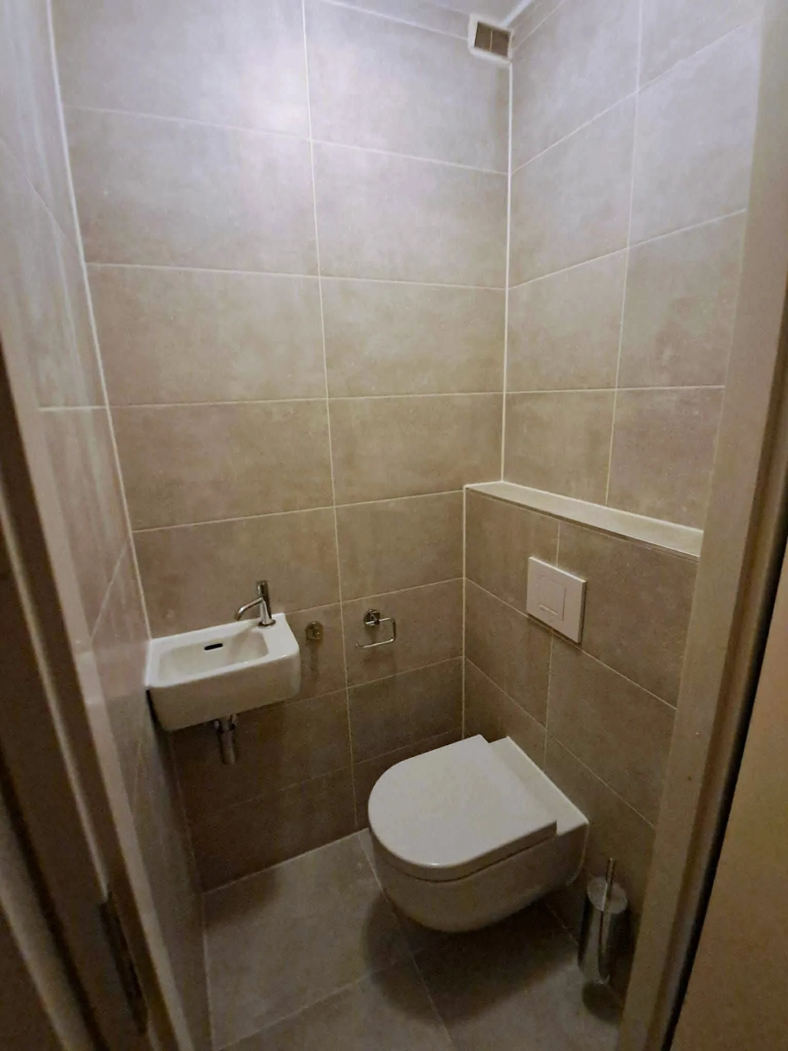 Toilet met een kleine fontein, houten accentwand en lichte tegels
