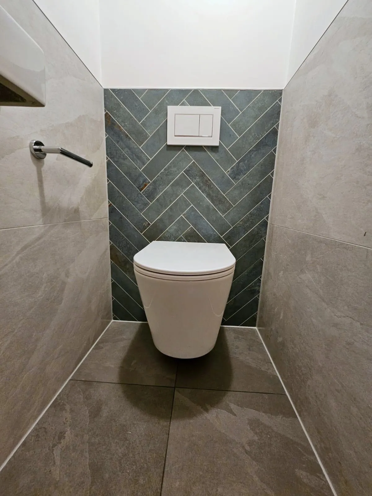 Toiletruimte met een achterwand van groene visgraattegels, een zwevend toilet met een wit bedieningspaneel en zijwanden in natuursteenlook