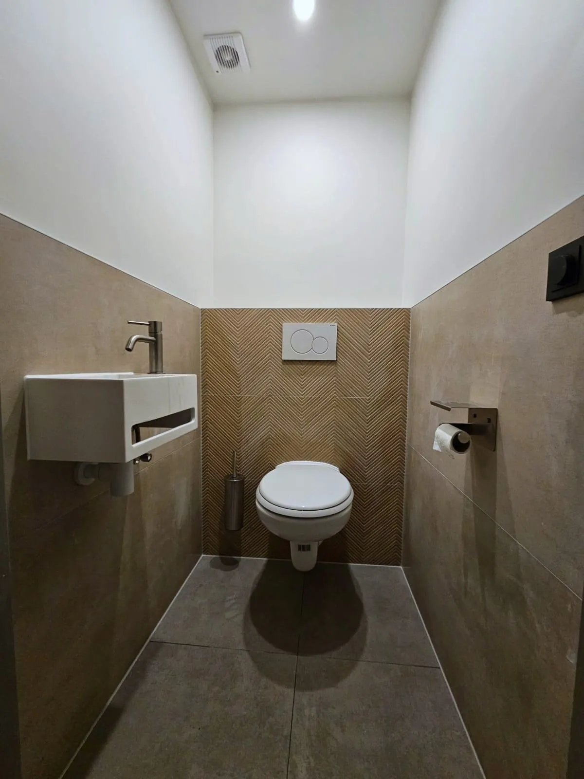 Toiletruimte met een achterwand in houtlook visgraat, een zwevend toilet en een witte fontein met een rvs kraan