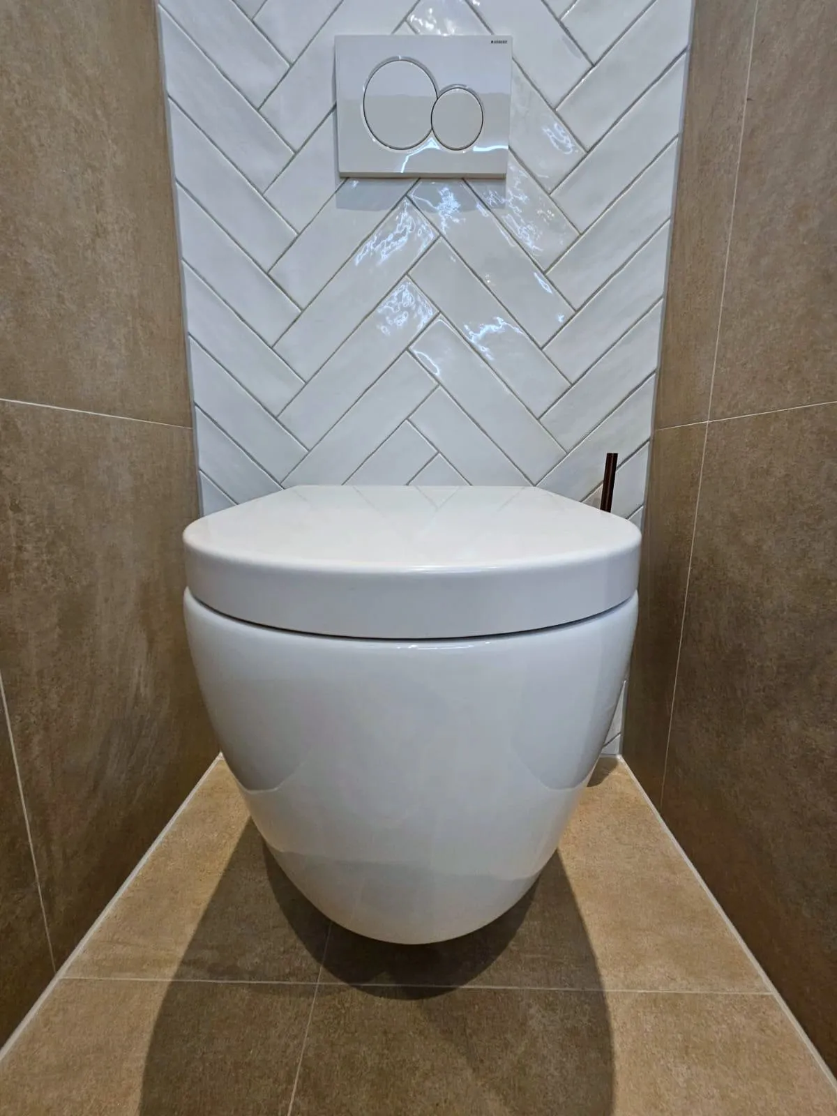 Zwevend toilet voor een achterwand van glanzende witte tegels in visgraat, met een wit bedieningspaneel erboven