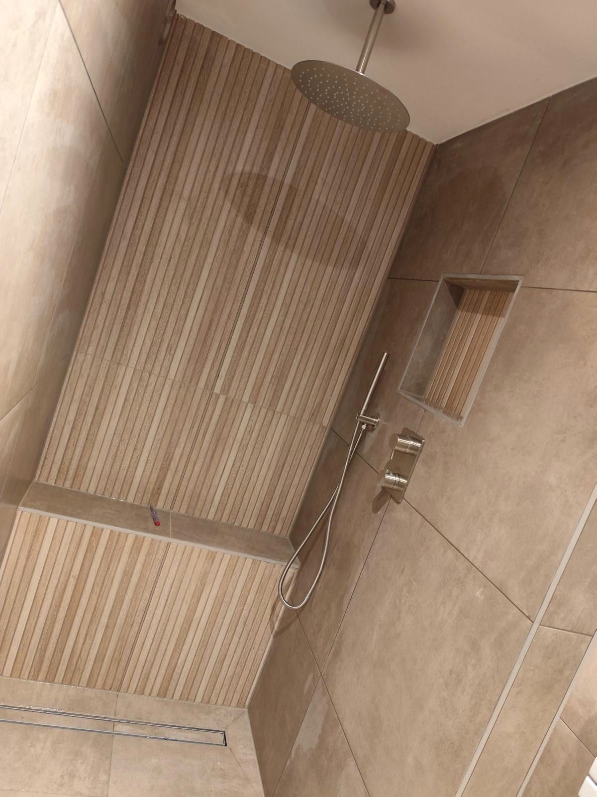 Doucheruimte met ribbelpanelen in houtlook, een regendouche aan het plafond en een verdiepte nis bekleed met ribbeltegel