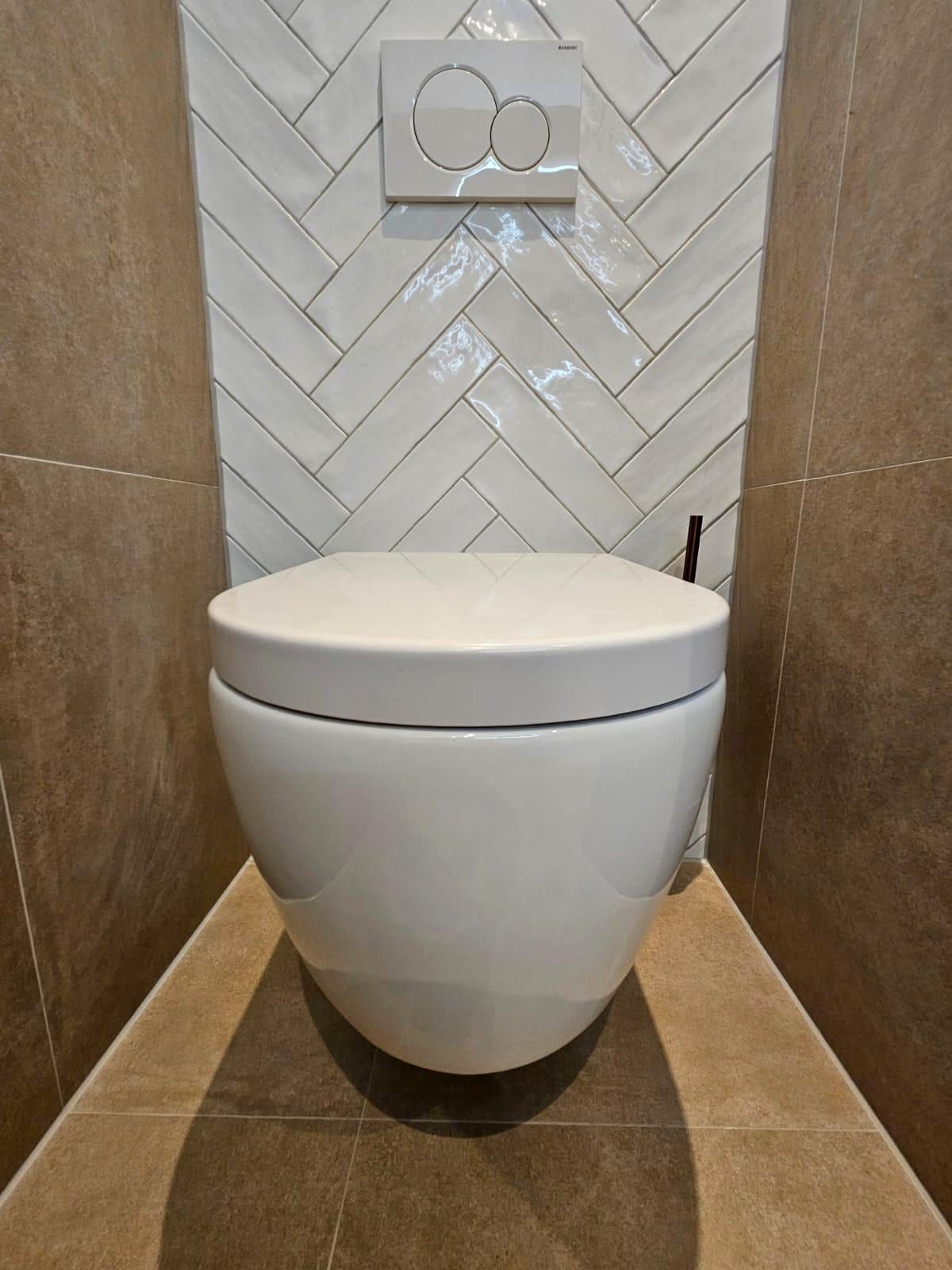 Zwevend toilet tegen een paneel van witte visgraattegel, met warme bruine tegels ernaast en een witte bedieningsplaat