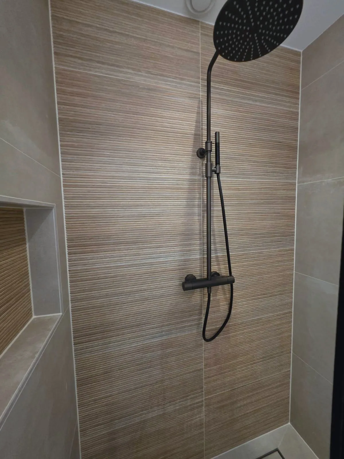 Zwarte regendouche met een thermostaatkraan voor een wand van houtlook ribbeltegels, met een nis in de zijwand